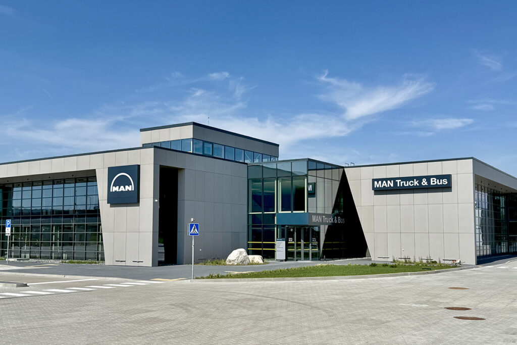 Eine flache Halle mit Glaswand steht auf einem Platz.