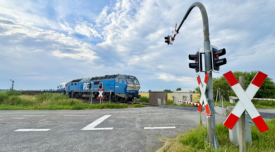 Ein Zug fährt über einen mit einer Ampel gesicherten Bahnübergang.