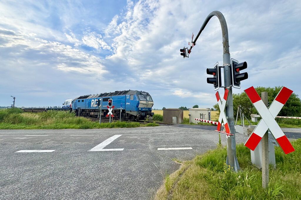 Ein Zug fährt über einen mit einer Ampel gesicherten Bahnübergang.