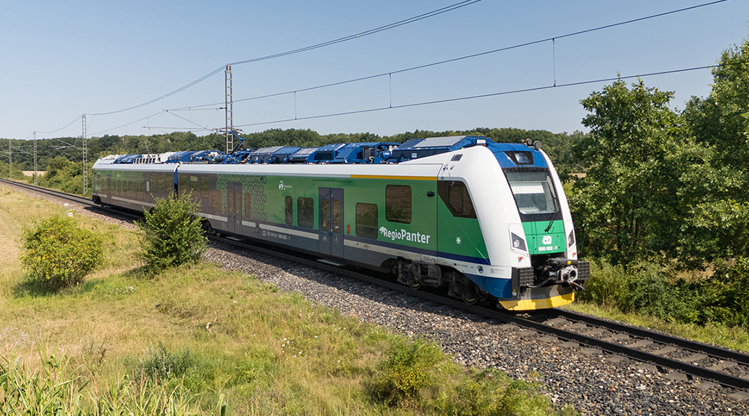 Ein Triebzug fährt auf einer Strecke vor Bäumen entlang.