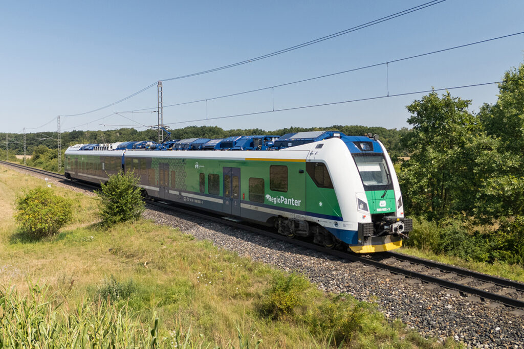 Ein Triebzug fährt auf einer Strecke vor Bäumen entlang.