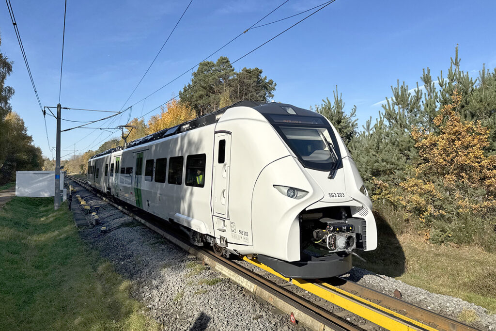 Ein Triebzug fährt auf einem Testgleis zwischen Bäumen entlang.