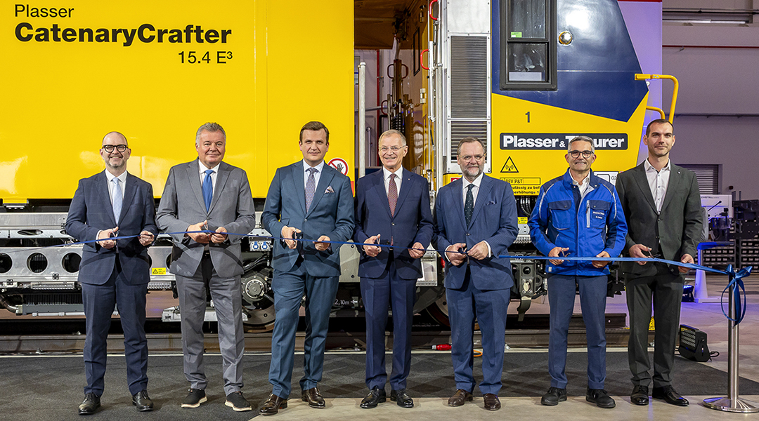 Mehrere Personen stehen vor einer Gleisbau-Maschine.