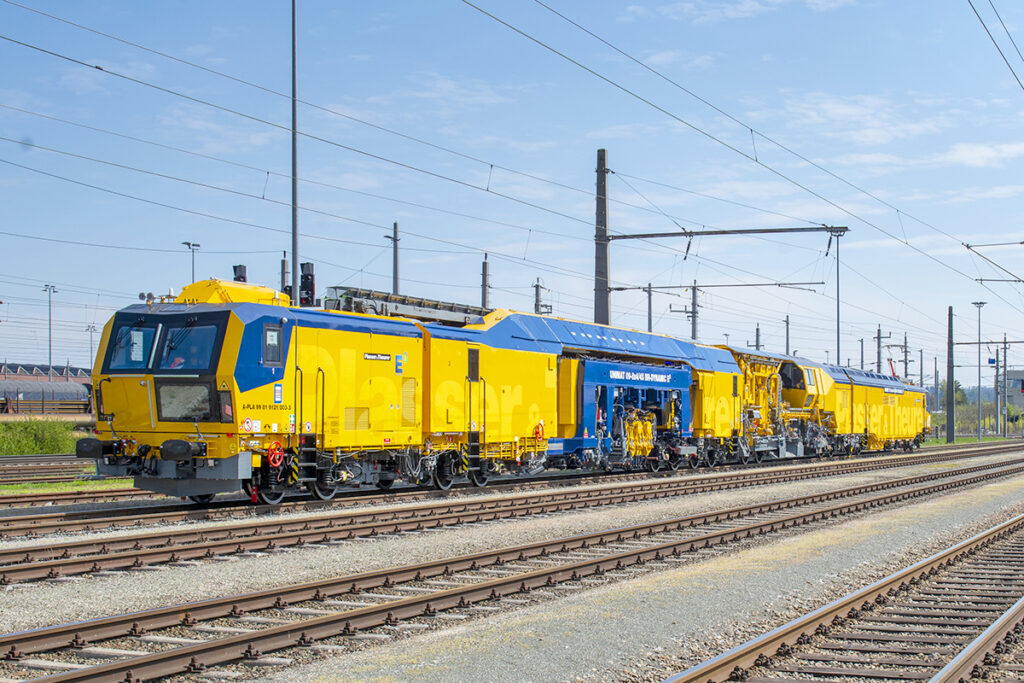 Eine lange Gleisbaumaschine steht auf einem Gleis.