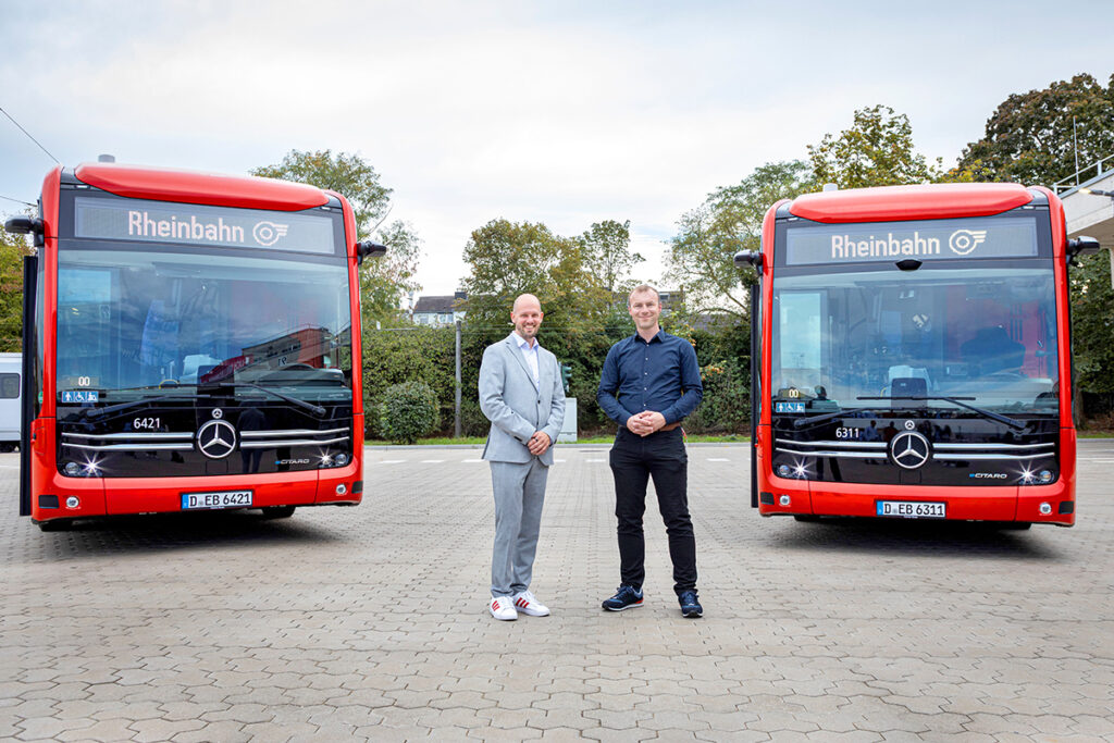 Zwei Personen stehen zwischen zwei neuen Elektrobussen.