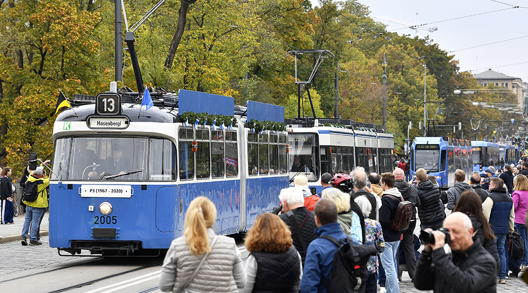 Mehrere Straßenbahnen fahren zwischen vielen Menschen hintereinander.