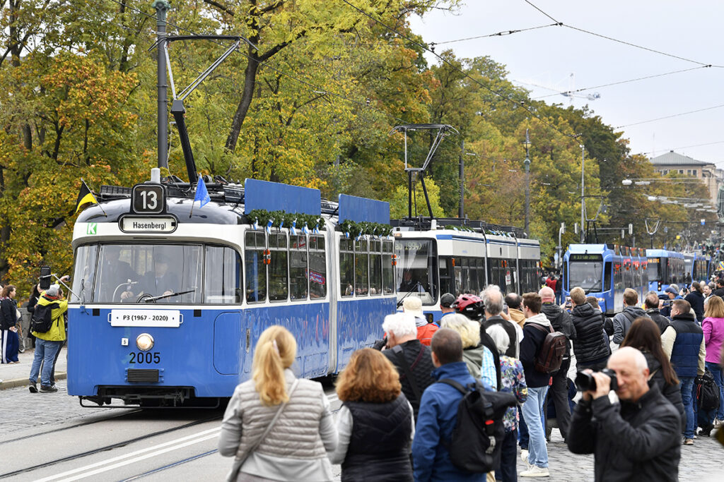 Mehrere Straßenbahnen fahren zwischen vielen Menschen hintereinander.