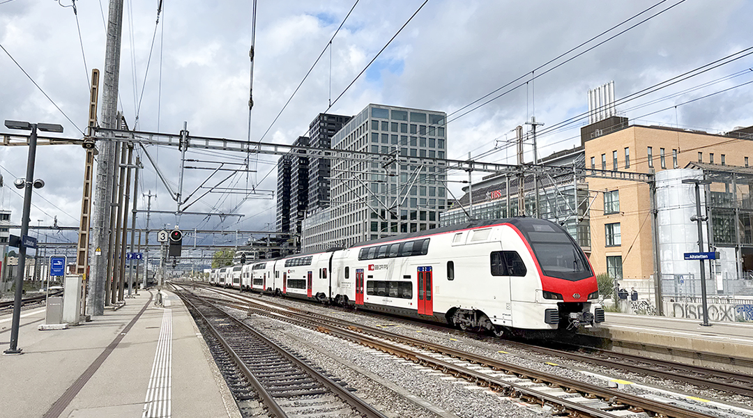 Ein Doppelstockzug fährt an Hochhäusern entlang.