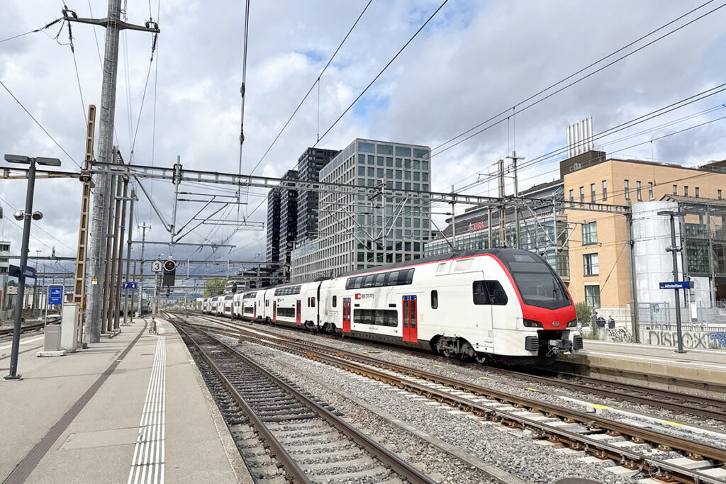 Ein Doppelstockzug fährt an Hochhäusern entlang.