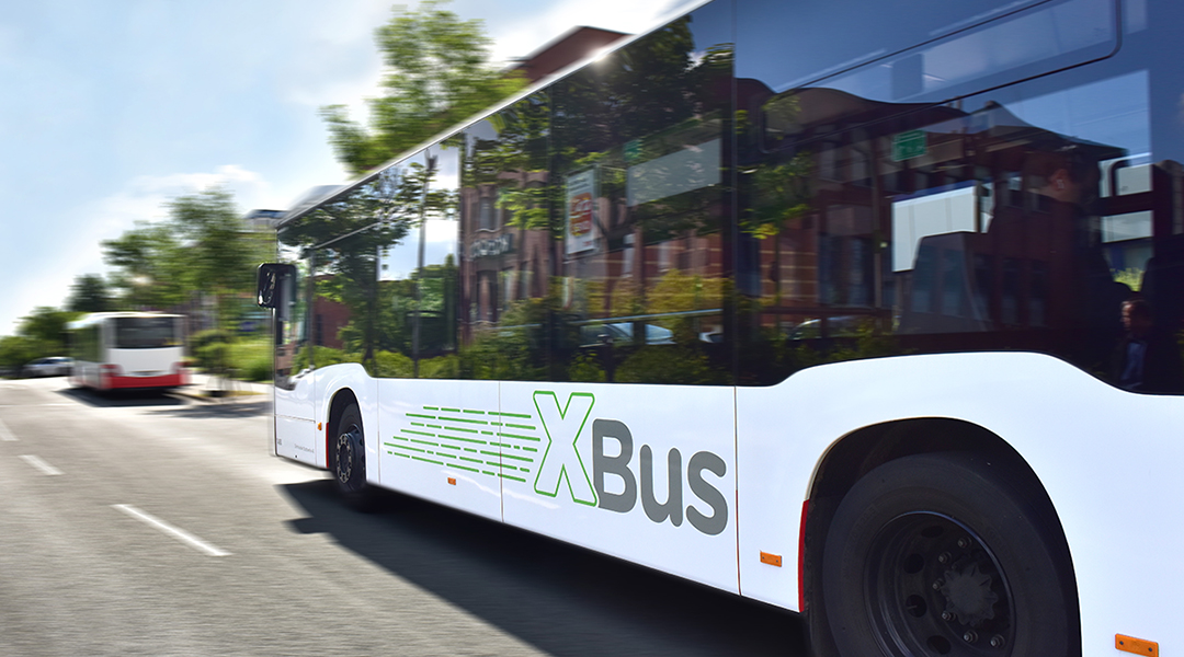 Ein Niederflurbus mit der Aufschrift XBus auf der Seite fährt auf einer Straße.