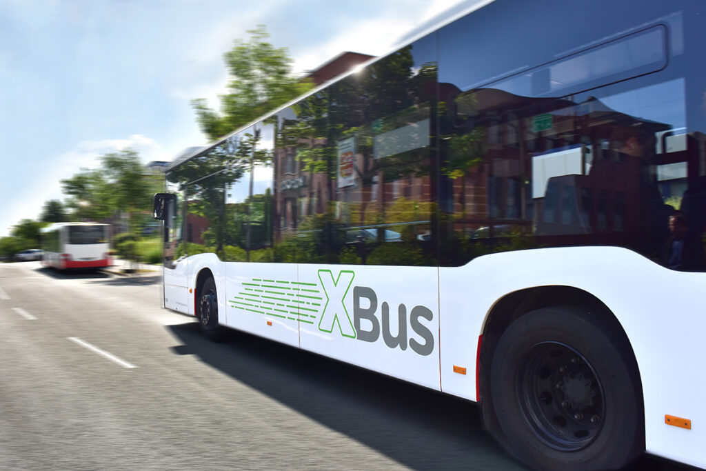 Ein Niederflurbus mit der Aufschrift XBus auf der Seite fährt auf einer Straße.
